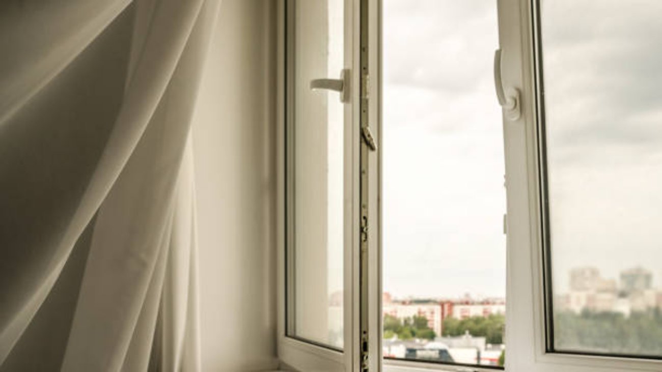 transparent white curtain blows on open plastic window in room of city home